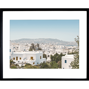 Coastal Wall Art featuring white coastal buildings against a backdrop of similar white building, rolling hills and blue skyline in black frame