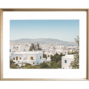 Coastal Wall Art featuring white coastal buildings against a backdrop of similar white building, rolling hills and blue skyline in cashew frame