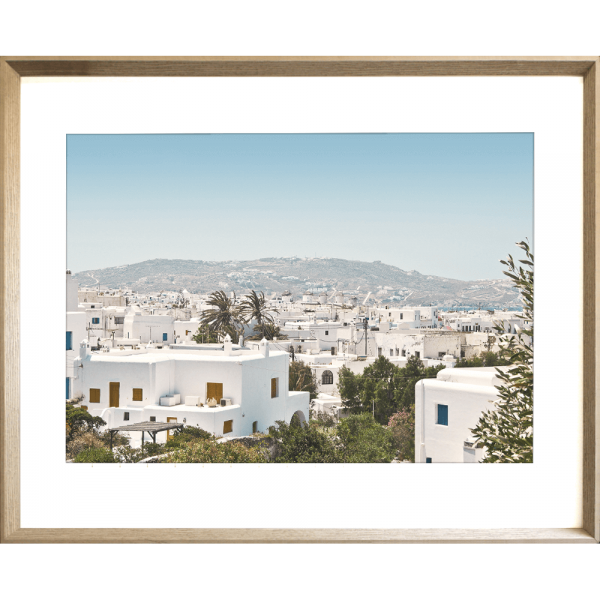 Coastal Wall Art featuring white coastal buildings against a backdrop of similar white building, rolling hills and blue skyline in cashew frame