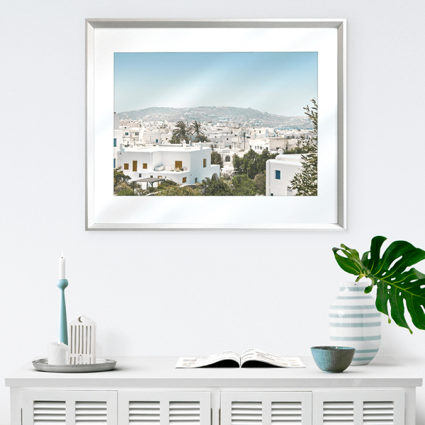 Coastal Wall Art against a white wall featuring white coastal buildings against a backdrop of similar white building, rolling hills and blue skyline wall mounted