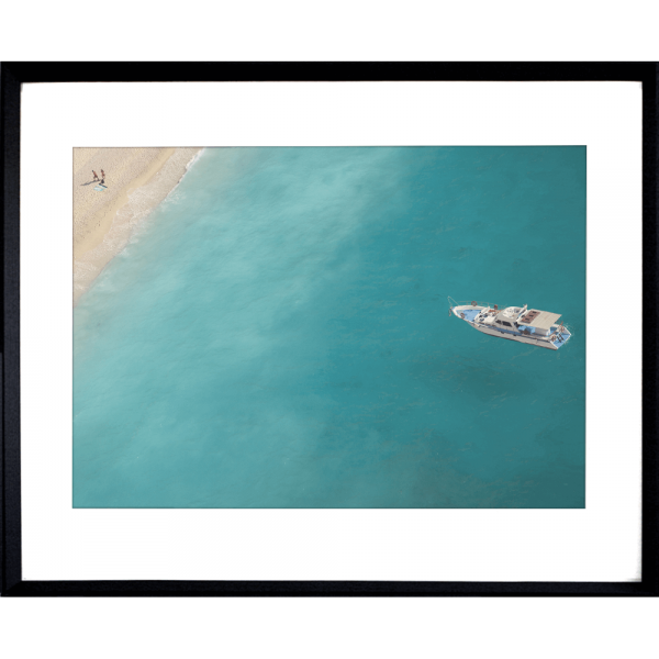 Black framed Coastal Wall Art featuring a dark to light aqua ocean and a single white boat drifting towards the shoreline.