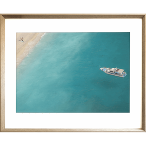 Gold framed Coastal Wall Art featuring a dark to light aqua ocean and a single white boat drifting towards the shoreline.