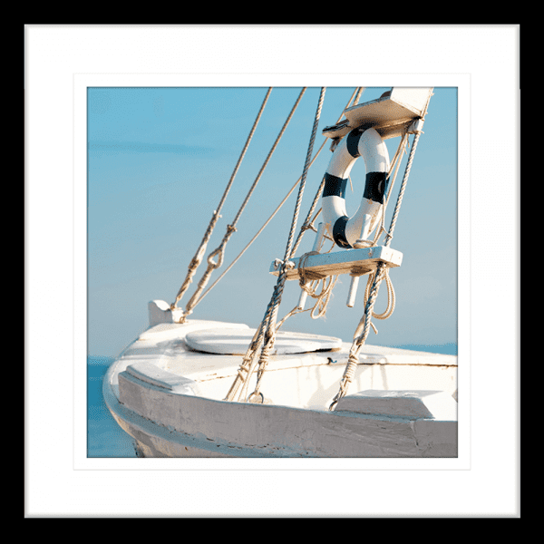 Black framed Nautical Wall Art, featuring a single crisp white sailing ship floating on a pristine sky-blue ocean, against a pale blue skyline