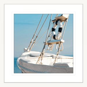 White framed Nautical Wall Art, featuring a single crisp white sailing ship floating on a pristine sky-blue ocean, against a pale blue skyline