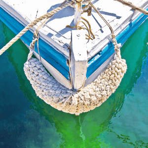 Unframed Nautical Wall Art Canvas, featuring the front section of white and light blue sailing ship floating on a pristine green ocean, moored with white nautical ropes.