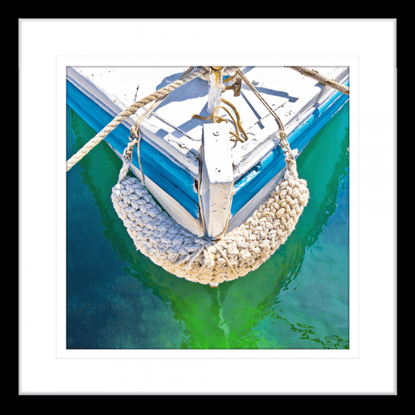 Black Framed Nautical Wall Art, featuring the front section of white and light blue sailing ship floating on a pristine green ocean, moored with white nautical ropes.