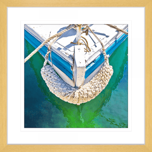 Gold Framed Nautical Wall Art, featuring the front section of white and light blue sailing ship floating on a pristine green ocean, moored with white nautical ropes.