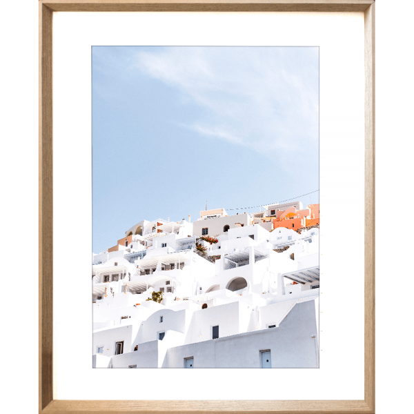 Gold framed Greek Island Photo featuring iconic European white coastal homes under a soothing pale blue skyline.