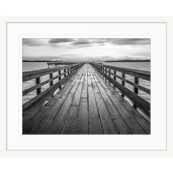 Black and white wall art features a long pier cascading into the deep ocean, with an array of white clouds overhead in a white frame