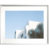 Silver framed Tropical Wall Art - The Weekender - Artist Collection, featuring striking a crisp white tropical hotel nestled amongst breezy palm trees, against a sky blue background. 