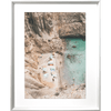 Silver framed Coastal Wall Art - Vacanza 01 – Studio Collection, Featuring a relaxing beach scene nestled within a cliff face. Clear aqua water with beach lovers sun baking in the sunshine.