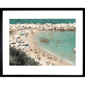 Black framed Coastal Wall Art Vacanza 02 – Studio Collection, featuring the European beach coastline with holiday beach lovers bathing in the sunshine.