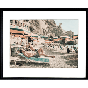 Black Framed Amalfi Coast Wall Art - Vacanza 05 – Studio Collection, featuring a relaxing coastal holiday beach scene with beach umbrellas in green and orange stripes, a tropical hotel and a peek at the crystal blue ocean.