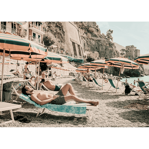 Stretched canvas Amalfi Coast Wall Art - Vacanza 05 – Studio Collection, featuring a relaxing coastal holiday beach scene with beach umbrellas in green and orange stripes, a tropical hotel and a peek at the crystal blue ocean.