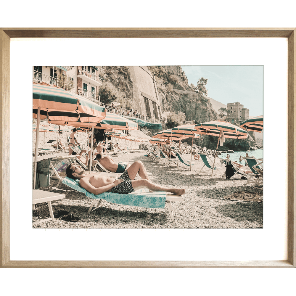 Gold framed Amalfi Coast Wall Art - Vacanza 05 – Studio Collection, featuring a relaxing coastal holiday beach scene with beach umbrellas in green and orange stripes, a tropical hotel and a peek at the crystal blue ocean.