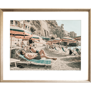 Gold framed Amalfi Coast Wall Art - Vacanza 05 – Studio Collection, featuring a relaxing coastal holiday beach scene with beach umbrellas in green and orange stripes, a tropical hotel and a peek at the crystal blue ocean.