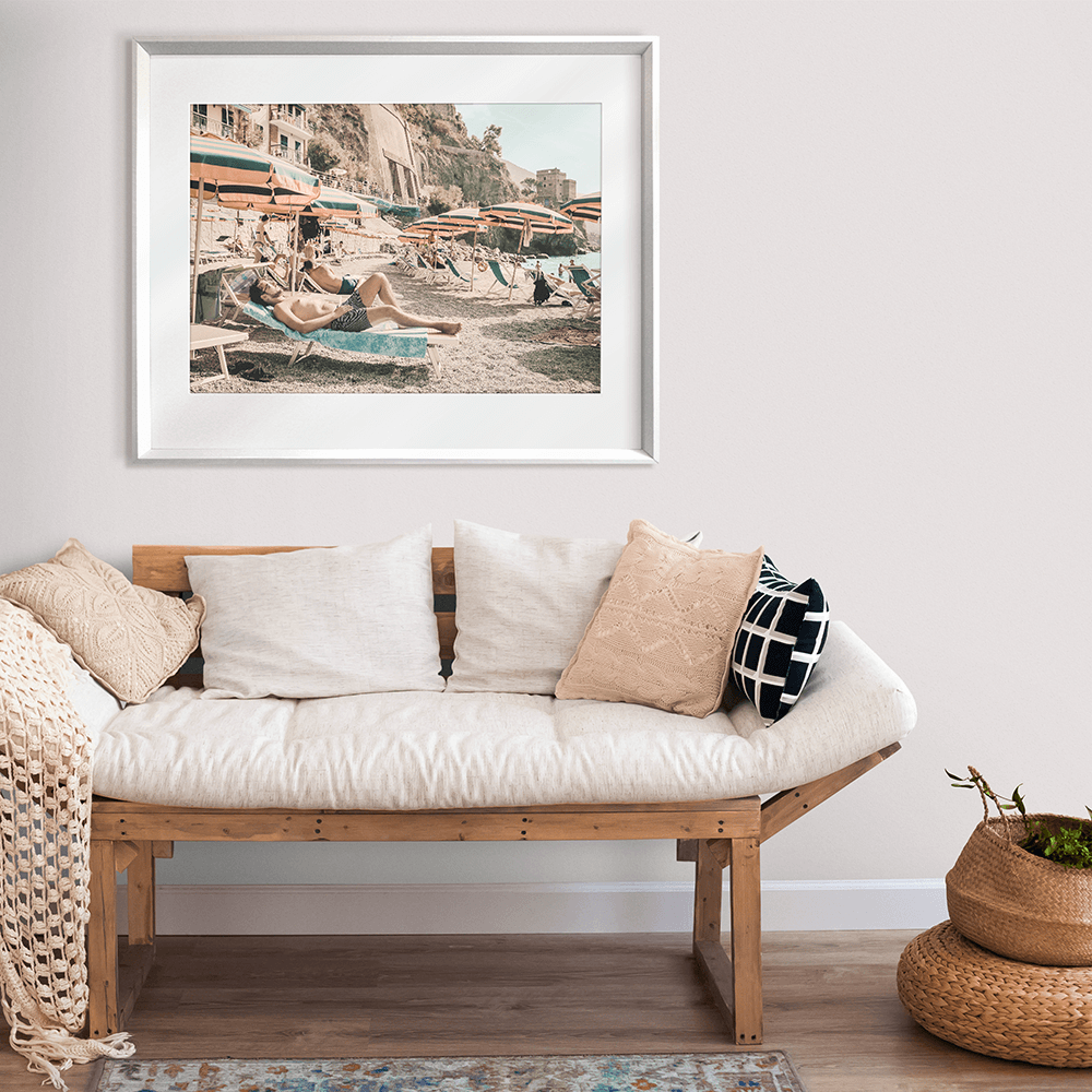 Coastal living with a silver framed Amalfi Coast canvas, featuring a relaxing coastal holiday beach scene with beach umbrellas in green and orange stripes, a tropical hotel and a peek at the crystal blue ocean.