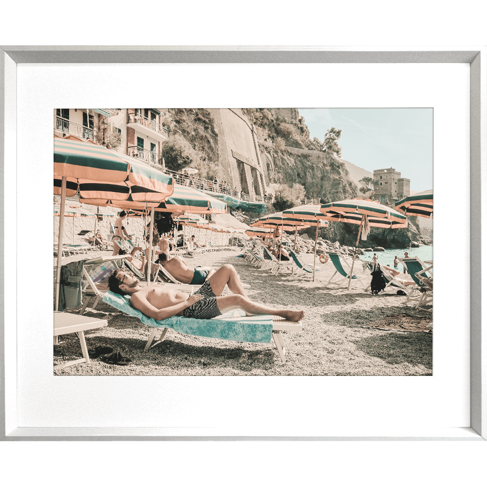 Silver framed Amalfi Coast Wall Art - Vacanza 05 – Studio Collection, featuring a relaxing coastal holiday beach scene with beach umbrellas in green and orange stripes, a tropical hotel and a peek at the crystal blue ocean.